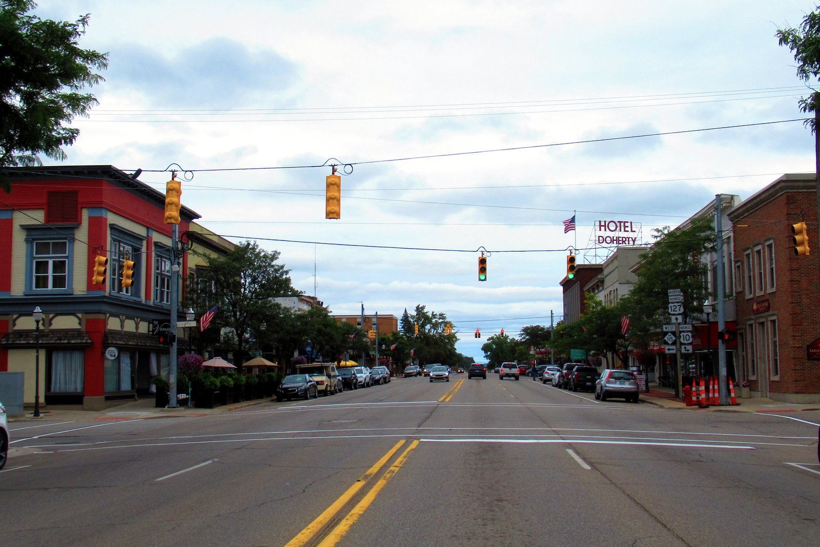 A wide main street in downtown Clare under cloudy skies, with brick storefronts on both sides, traffic lights strung across the road and a Hotel Doherty sign in the distance.