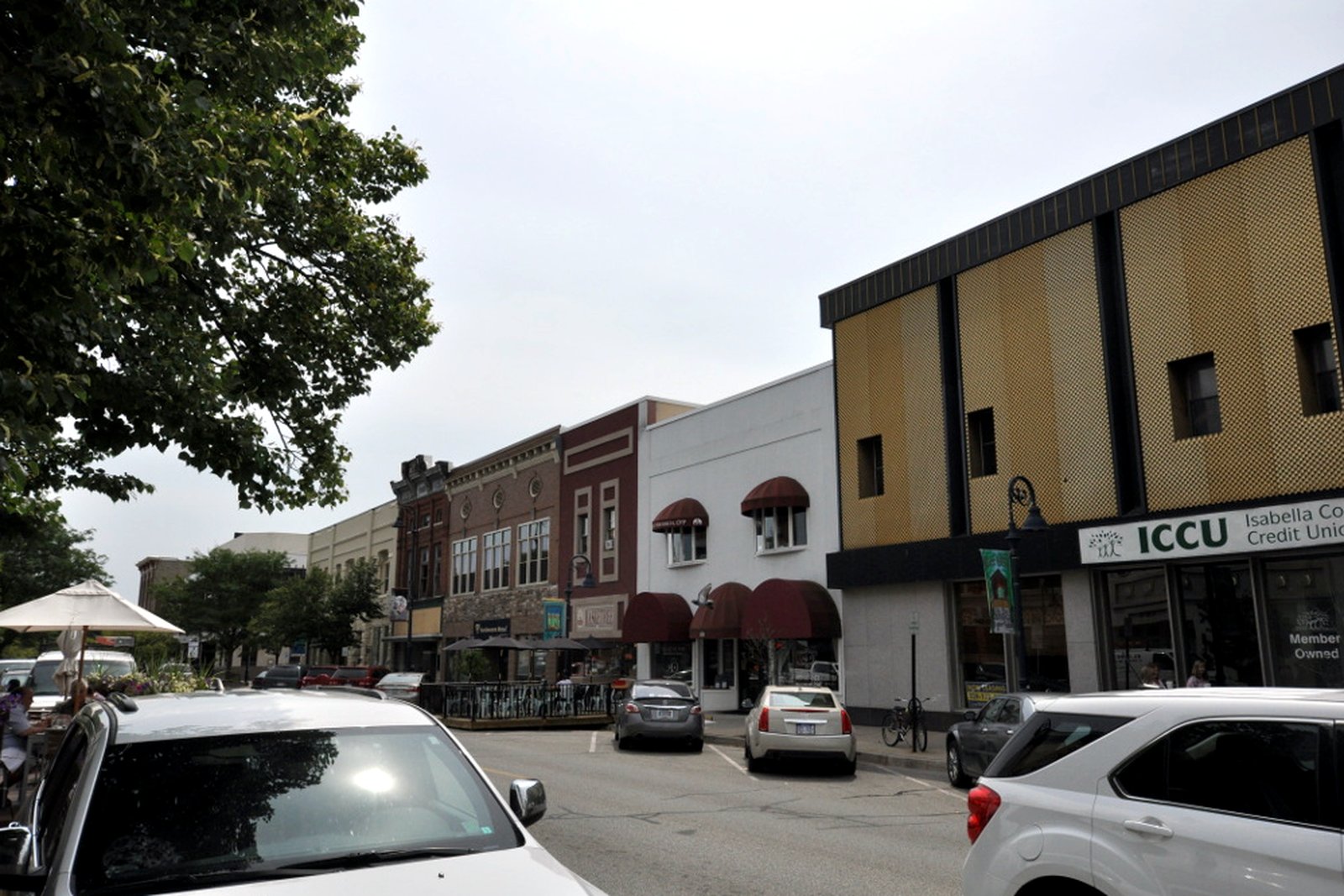 Brick commercial storefronts line a downtown Mount Pleasant sidewalk under a blue sky.