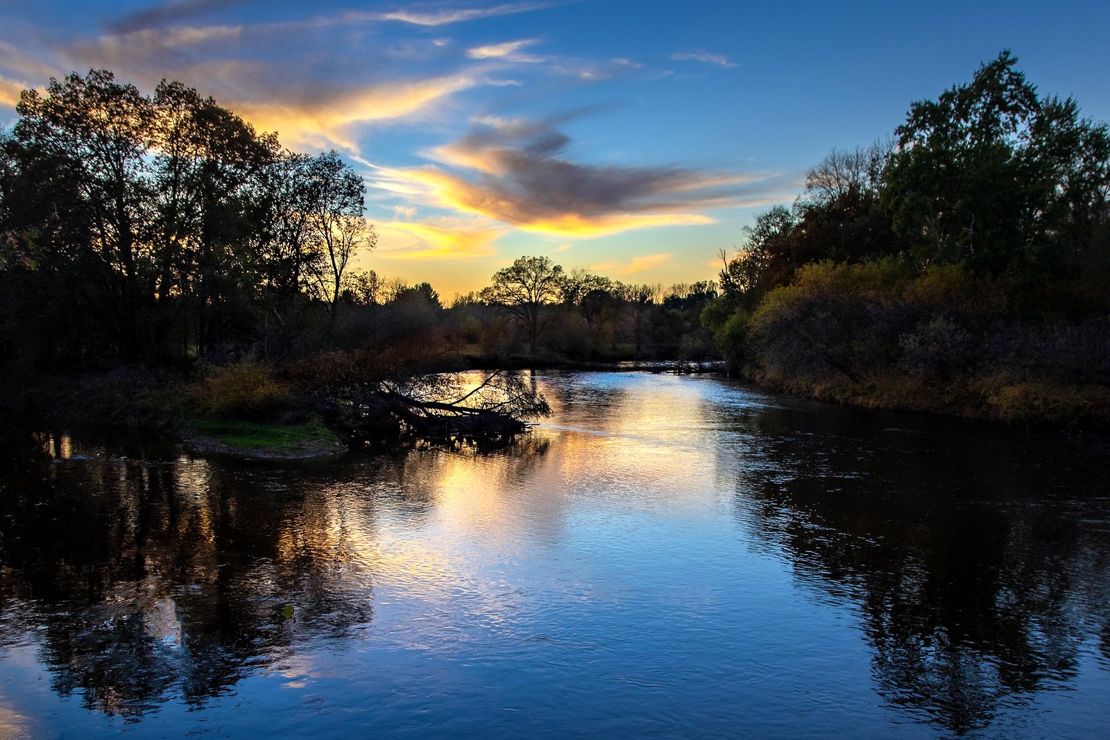 The Chippewa and Pine rivers meeting under a blue and gold sunset sky, with dark trees reflected in the water.