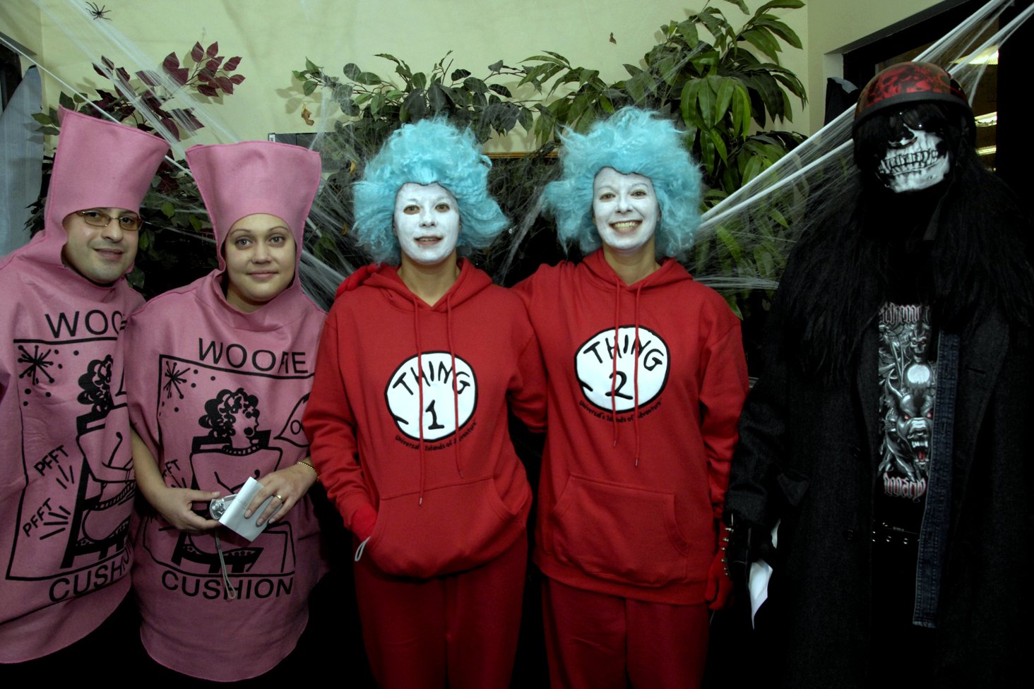 Five adults in Halloween costumes stand in a row indoors and pose for a group photo after a costume contest.