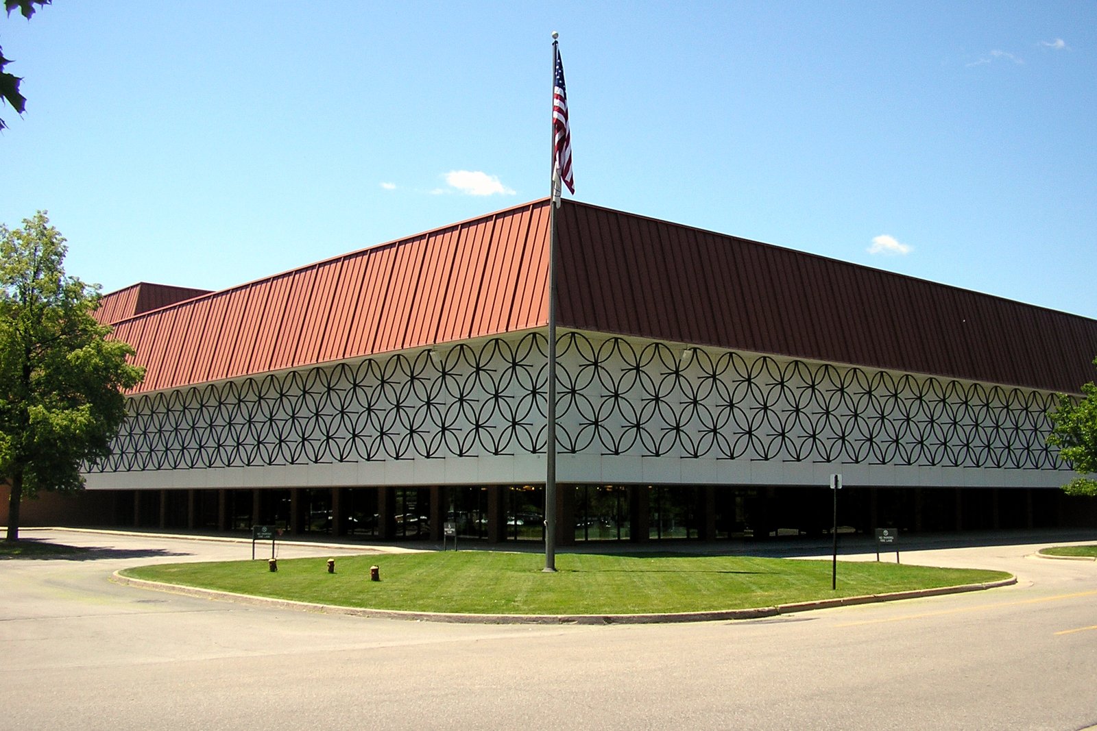 A modern glass-and-brick performing arts building with a tall tower and landscaping under a clear blue sky.