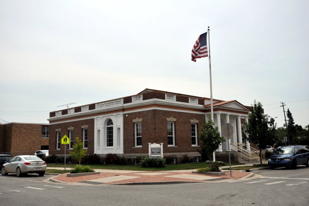A one-story red brick building with white columns and an American flag on a downtown corner in Mount Pleasant, Michigan.