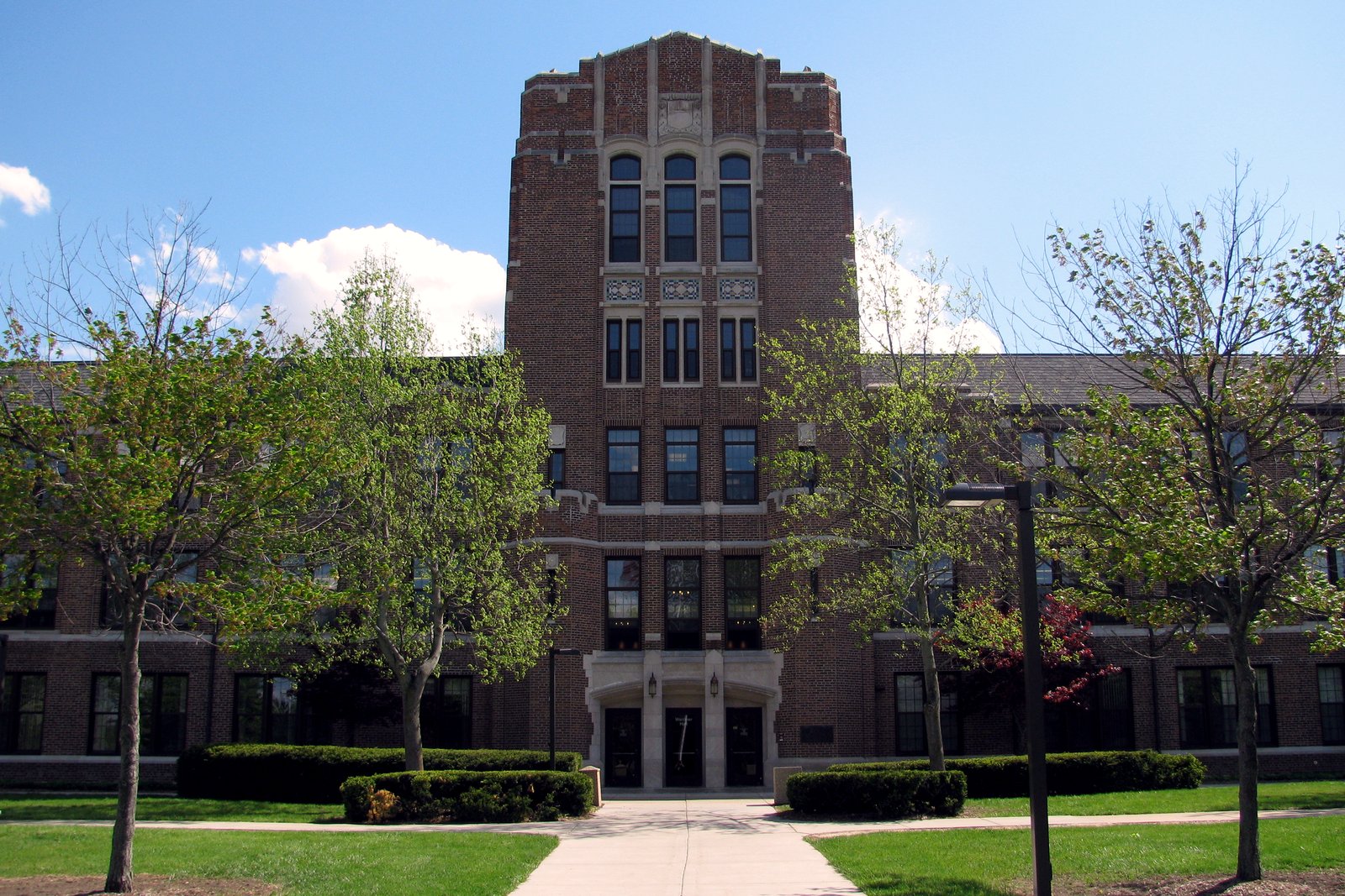 A tall brick tower rising above a long brick academic building, with green lawns and a sidewalk in front.