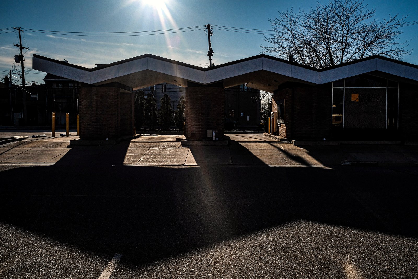 A quiet downtown corner in late-day sun, with a covered pavilion-style structure in silhouette and long shadows across an empty street.