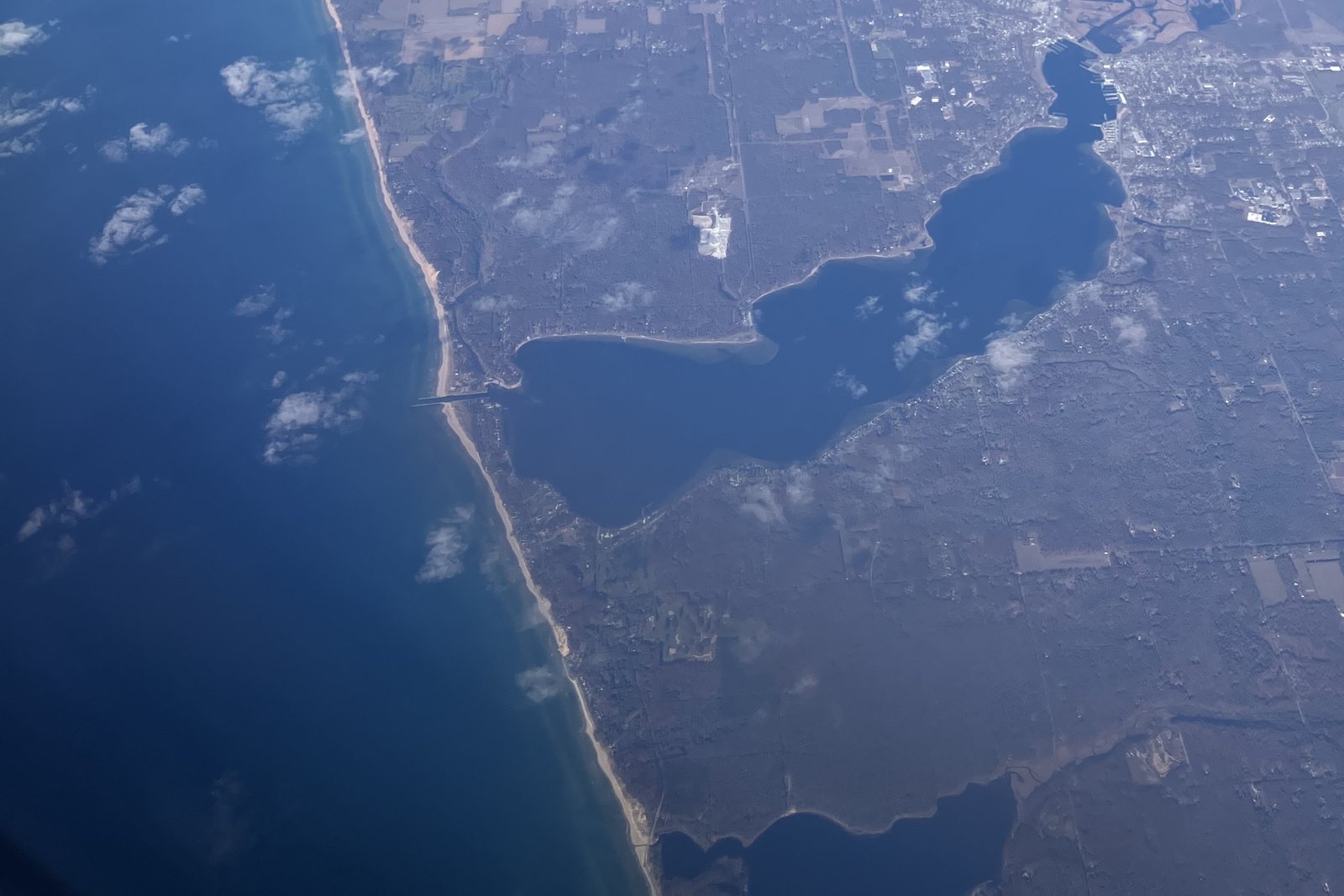 Aerial view looking north along the Lake Michigan shoreline in northern Muskegon County, with White Lake and the channel to Lake Michigan near the center, wooded land and farm fields, and part of Duck Lake at the bottom.