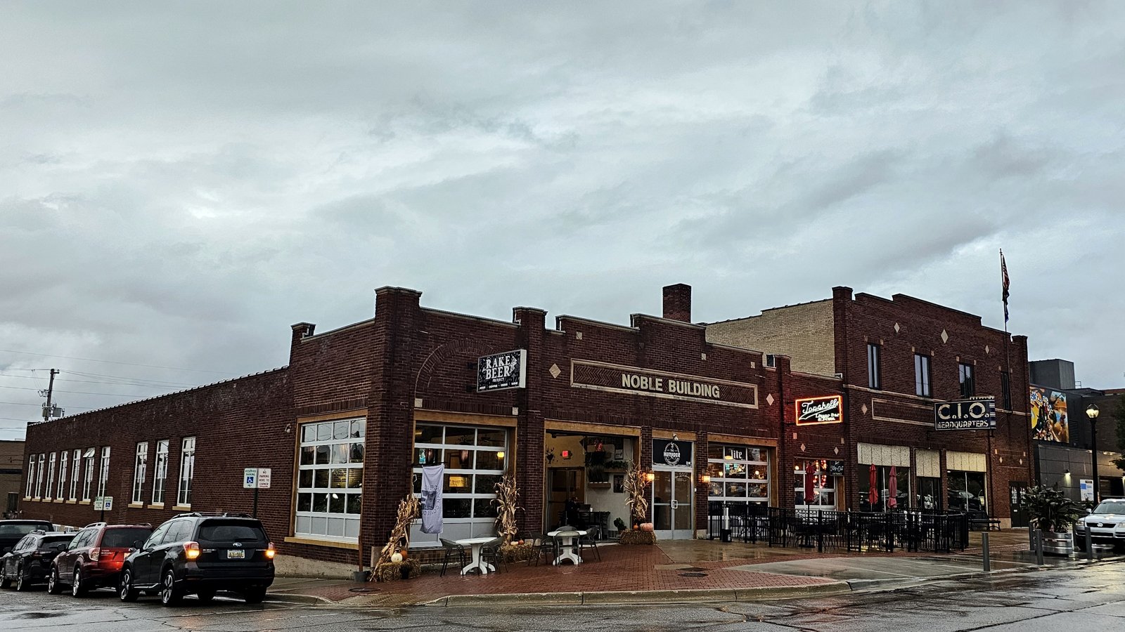 Downtown Muskegon storefronts on a wet autumn day with hay bales along the brick sidewalk.