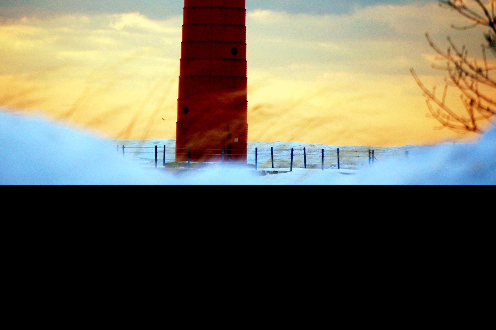 A red cylindrical lighthouse standing at the end of a pier on Lake Michigan under a clear blue sky.