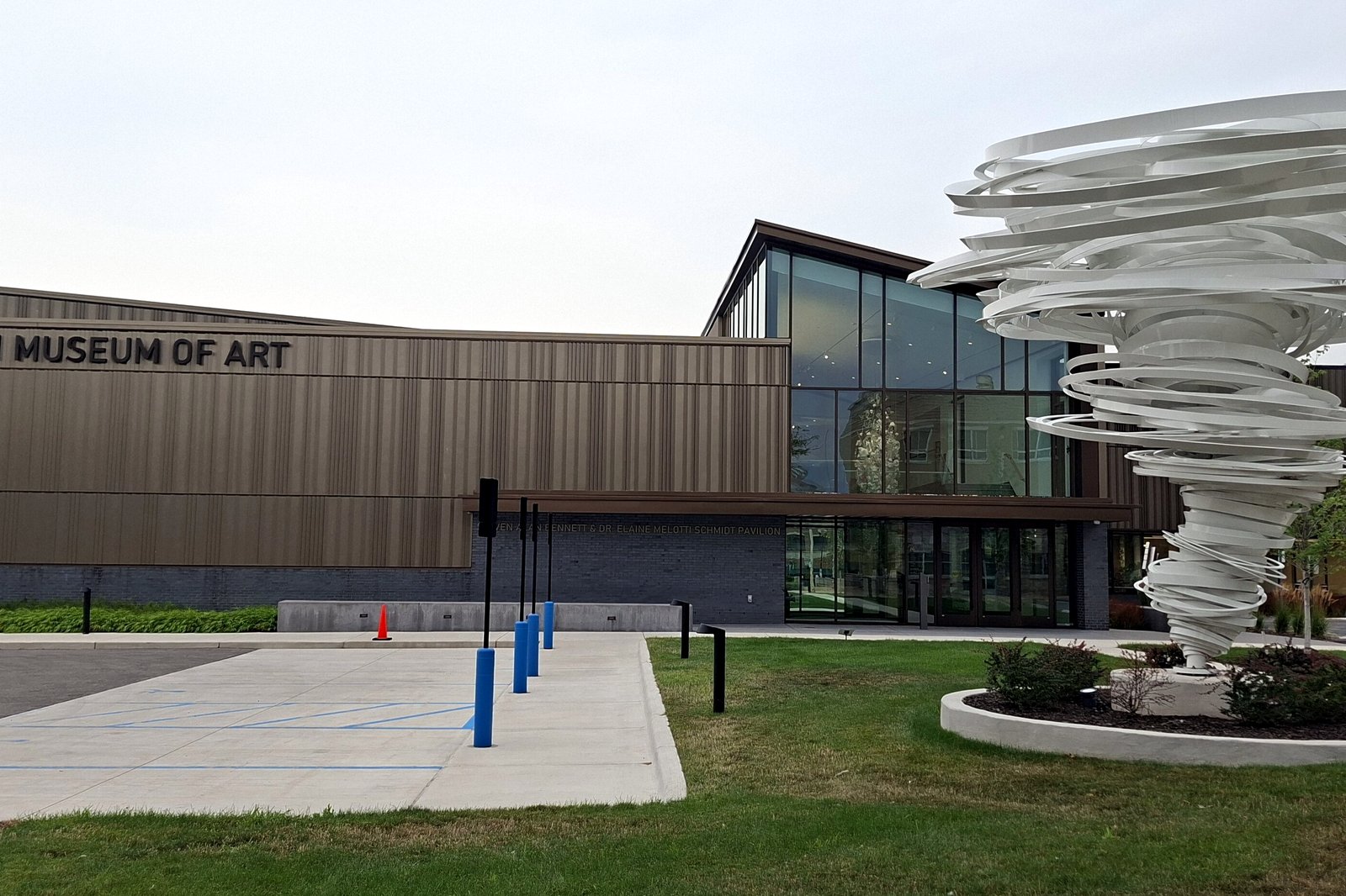 The modern entrance of the Muskegon Museum of Art, with wood-toned walls, a glass corner and a tall white spiraling sculpture beside a walkway.