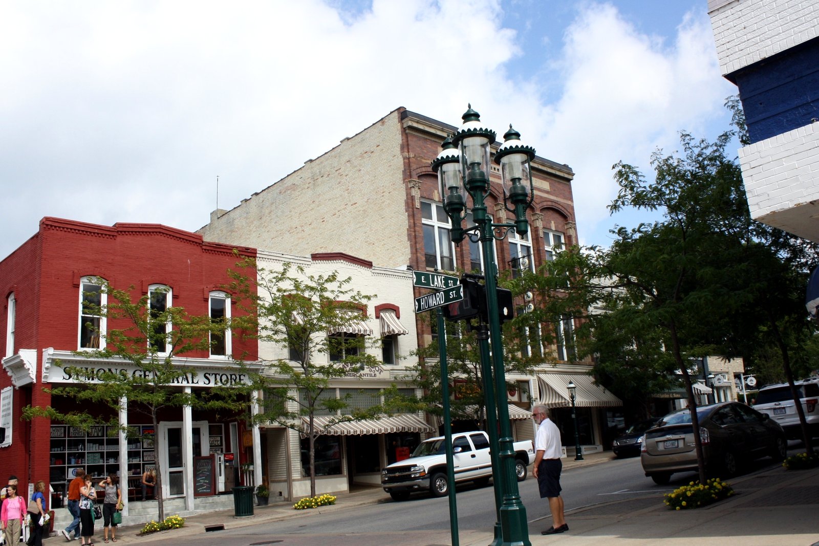 A row of older two-story brick storefronts with awnings along a downtown street corner on a sunny day.