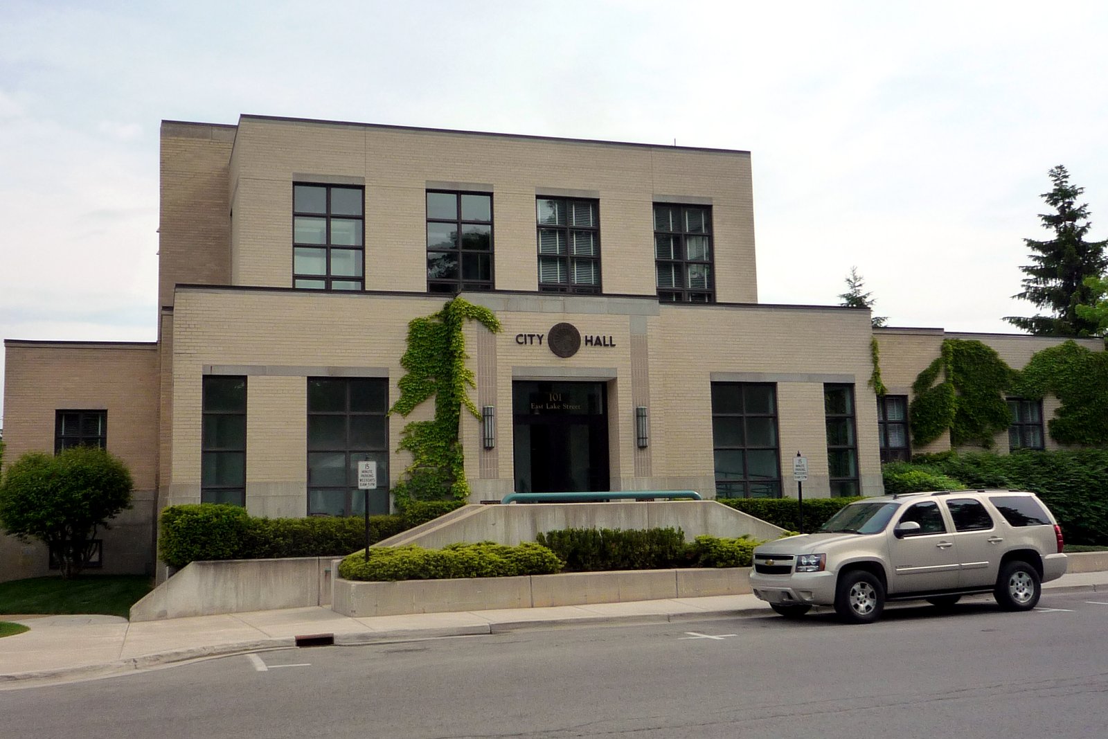 Petoskey City Hall, a two-story tan brick building with tall windows and ivy on the facade, seen from the street.
