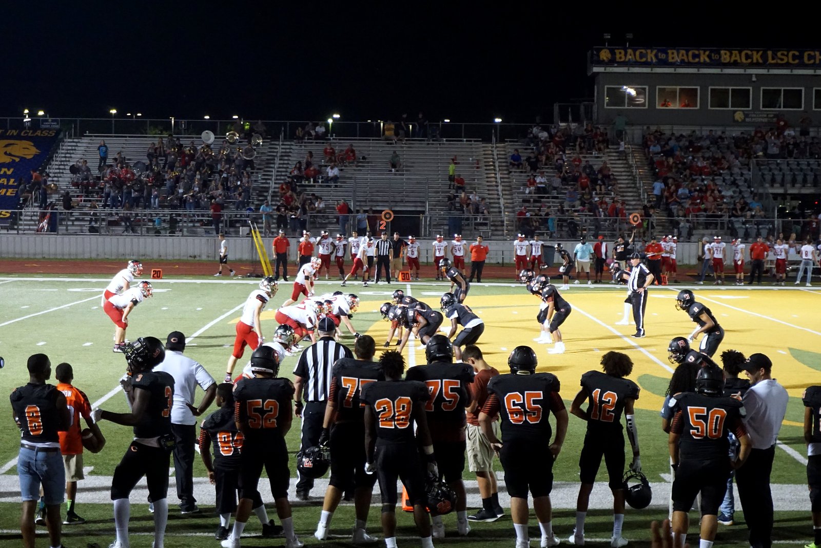 High school football players in dark and white uniforms at the line of scrimmage on a green field.