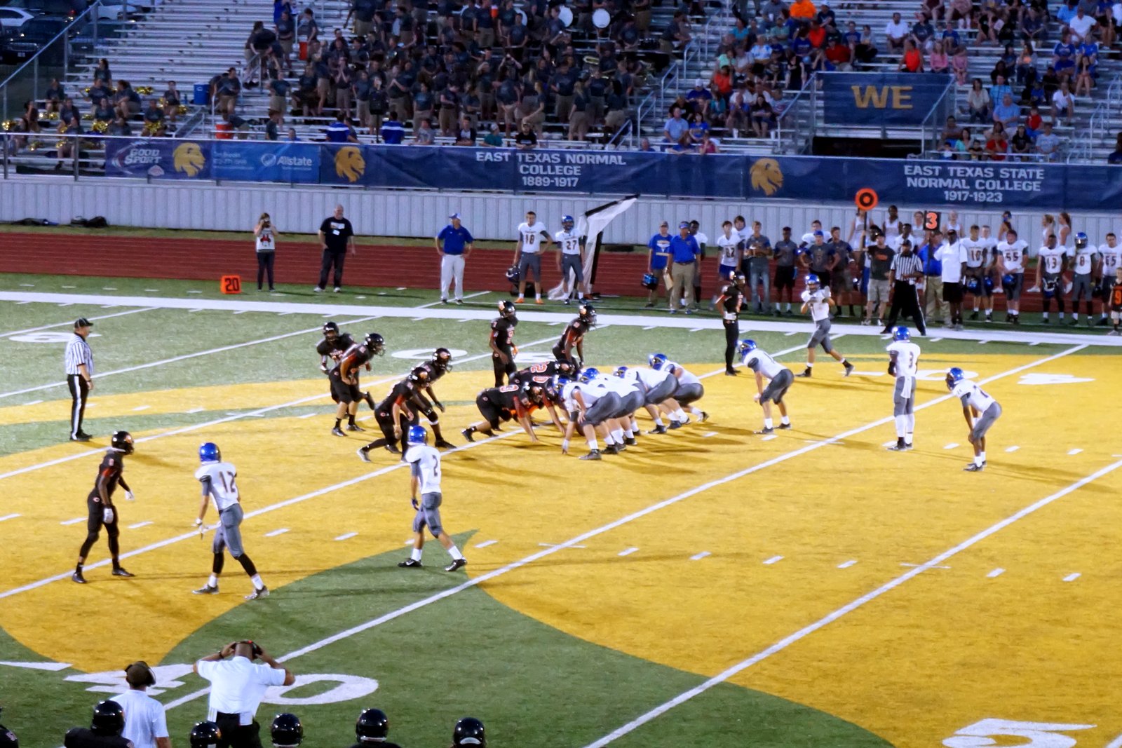 High school football teams in dark and white jerseys line up near the goal line under stadium lights as players watch from the sideline, in a file photo.