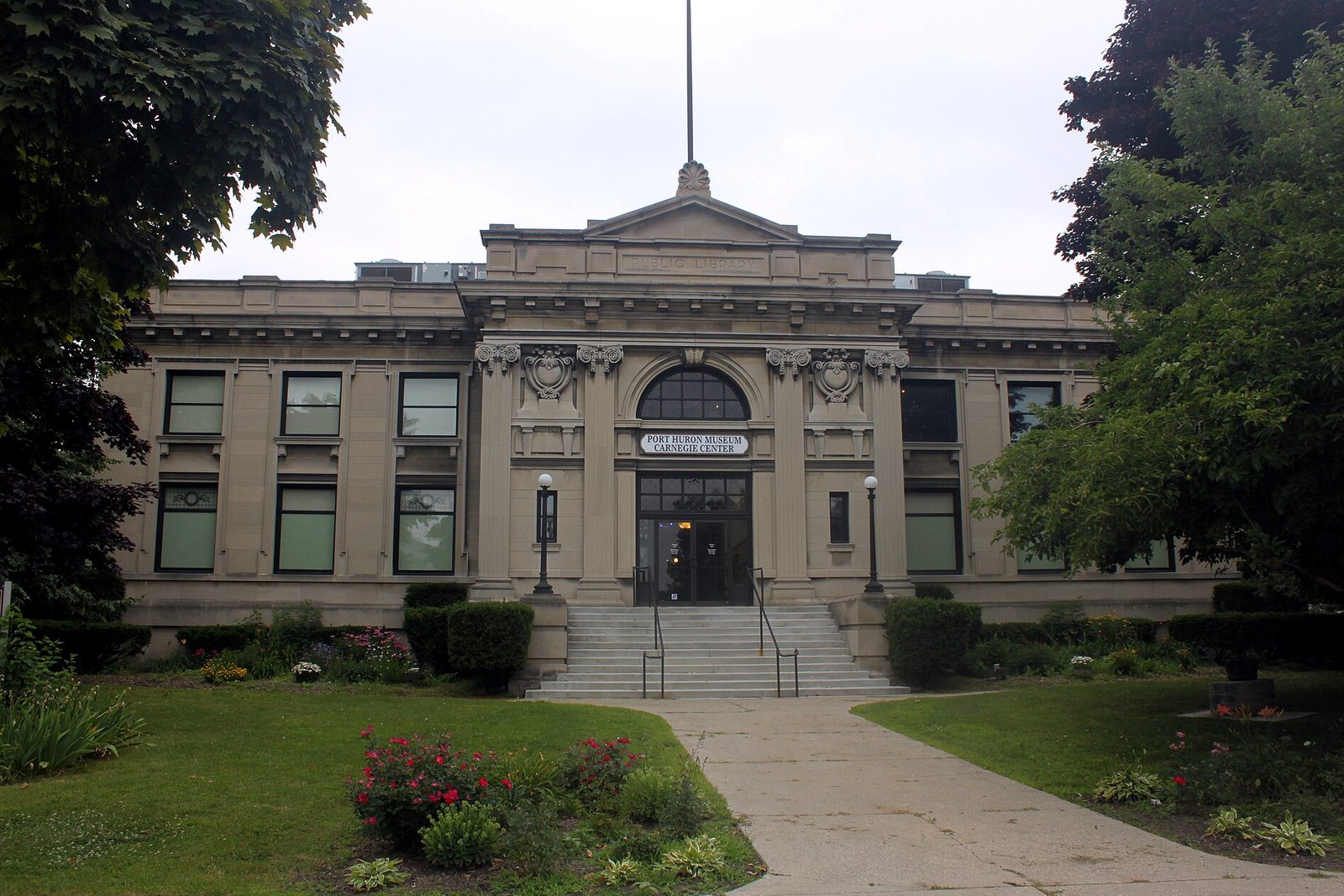 The stone front steps, arched window and columns of the Port Huron Museum’s Carnegie Center, framed by trees and a green lawn.