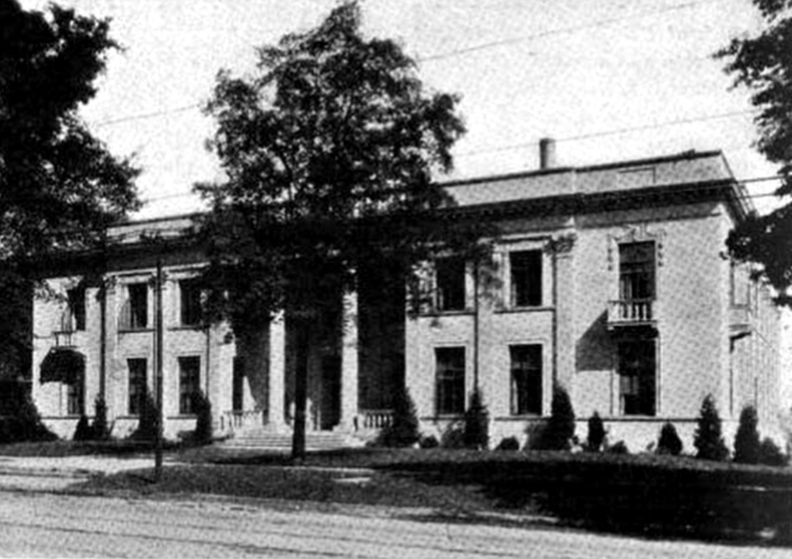 A black-and-white 1918 photograph of a broad two-story stone office building with tall windows and a columned entrance, set back behind a lawn and young trees along a street.