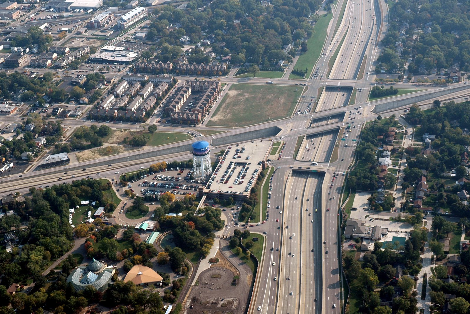 An aerial view of a sunken freeway crossing a wide boulevard, with neighborhoods, trees and a water tower beside the highway.