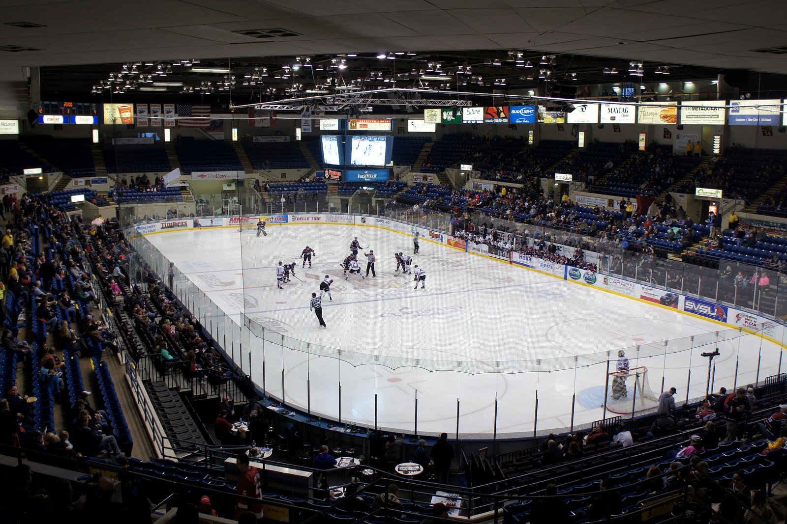 A hockey game in progress at the Dow Event Center in Saginaw, seen from high in the stands, with players at center ice, fans in blue seats and ad boards along the boards.