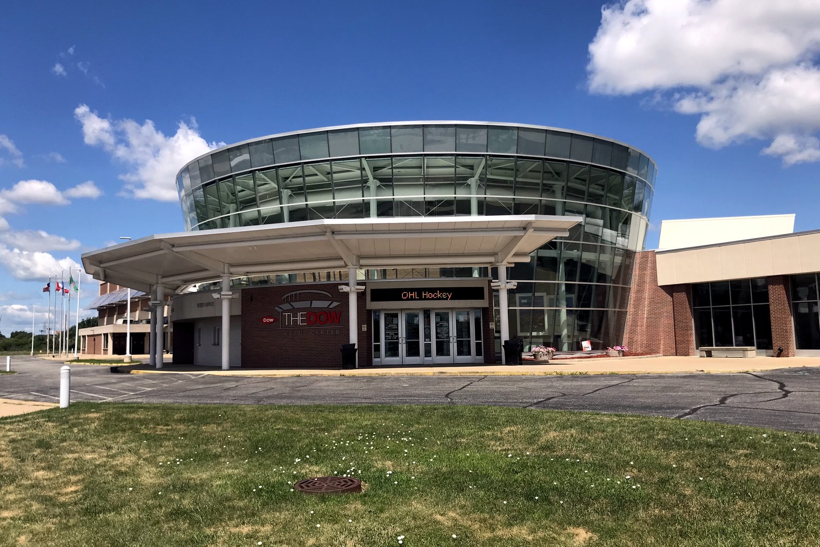 The Dow Event Center’s round glass-walled entrance and covered drop-off under a blue summer sky.