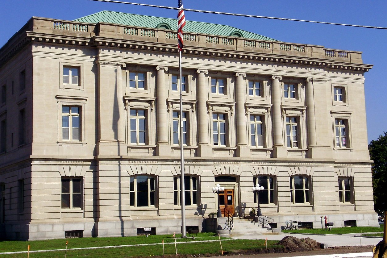 A two-story stone-and-brick civic building with tall windows and flags, Sault Ste. Marie City Hall.