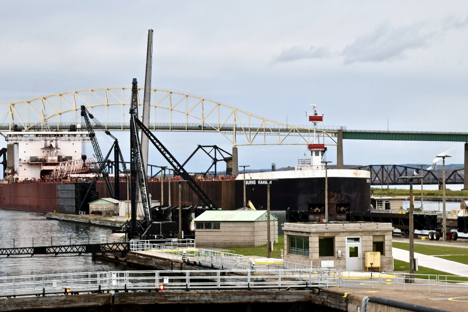 A long dark-red freighter slides into the Poe Lock at the Soo Locks, with lock walls and onlookers in the foreground.