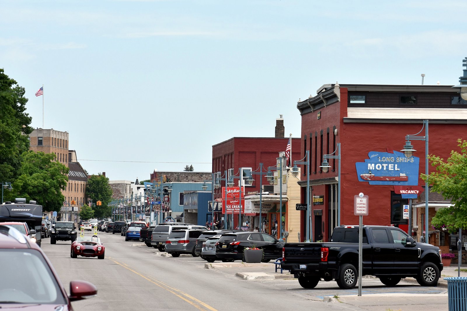 A downtown street with brick storefronts, parked pickup trucks and a red brick building under a blue sky.