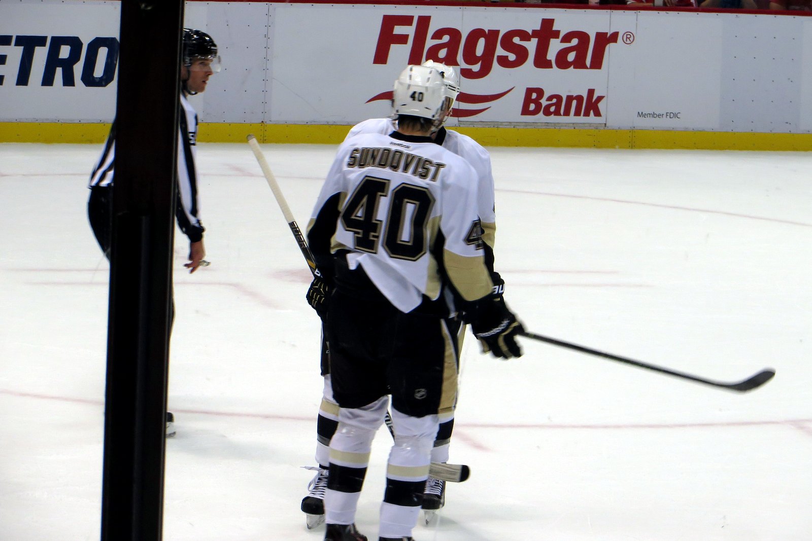 Two professional hockey players chase the puck along the boards during an exhibition overtime period in a large arena.