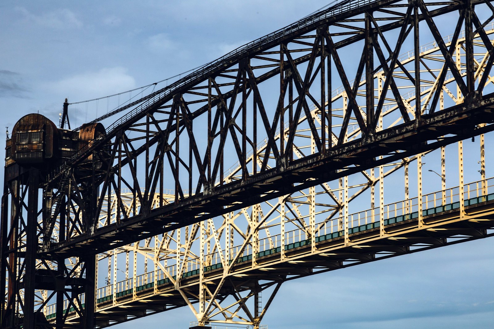 The steel truss spans of the Sault Ste. Marie International Bridge and the rail bridge in front of it, seen from below against a cloudy sky.