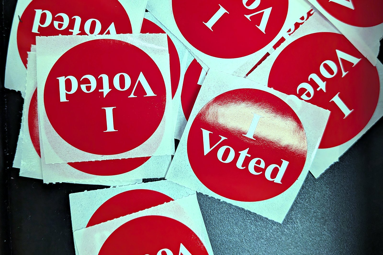 A scattered pile of round red I Voted stickers with white lettering.
