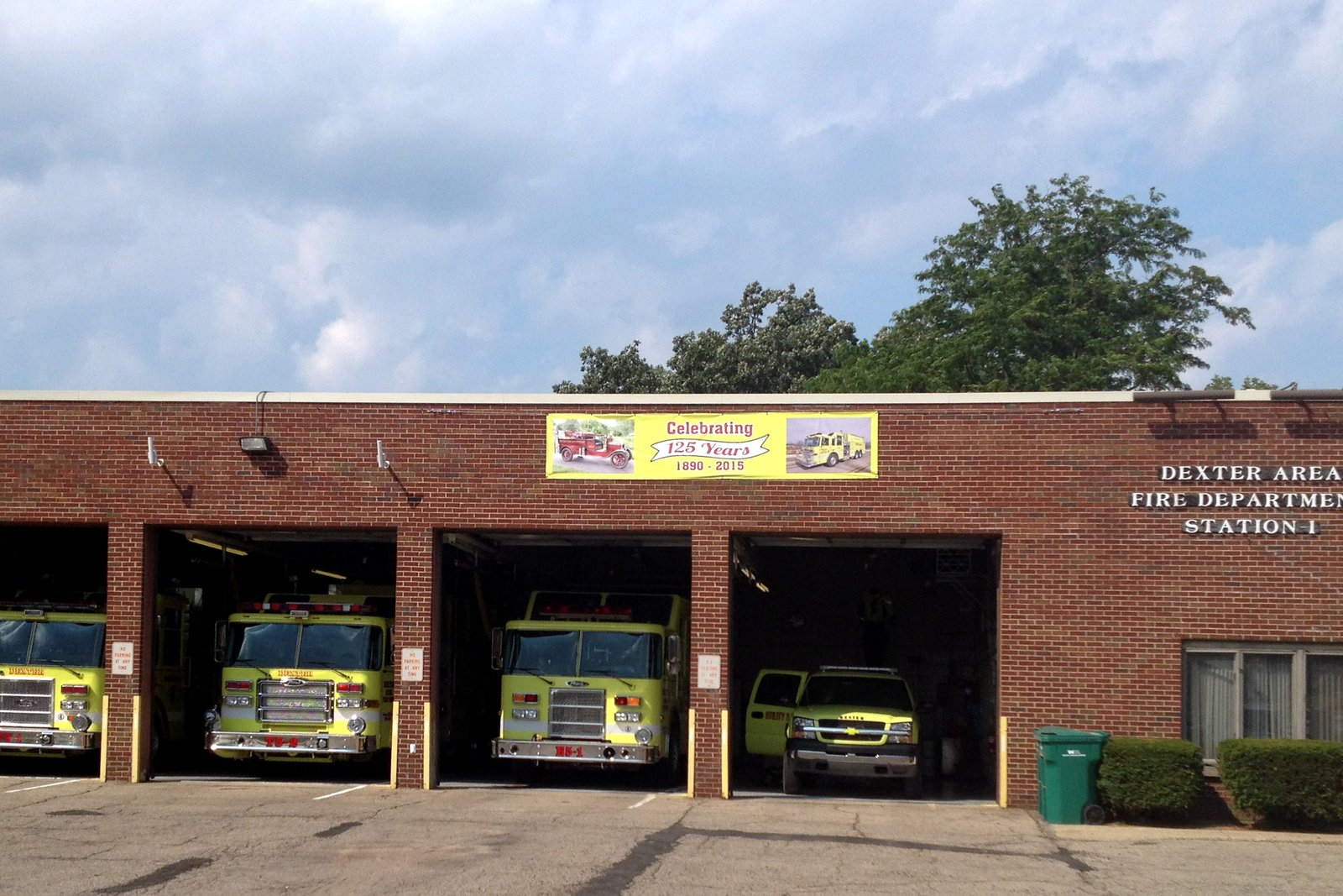 A brick fire station with four open bays holding yellow-green fire engines.