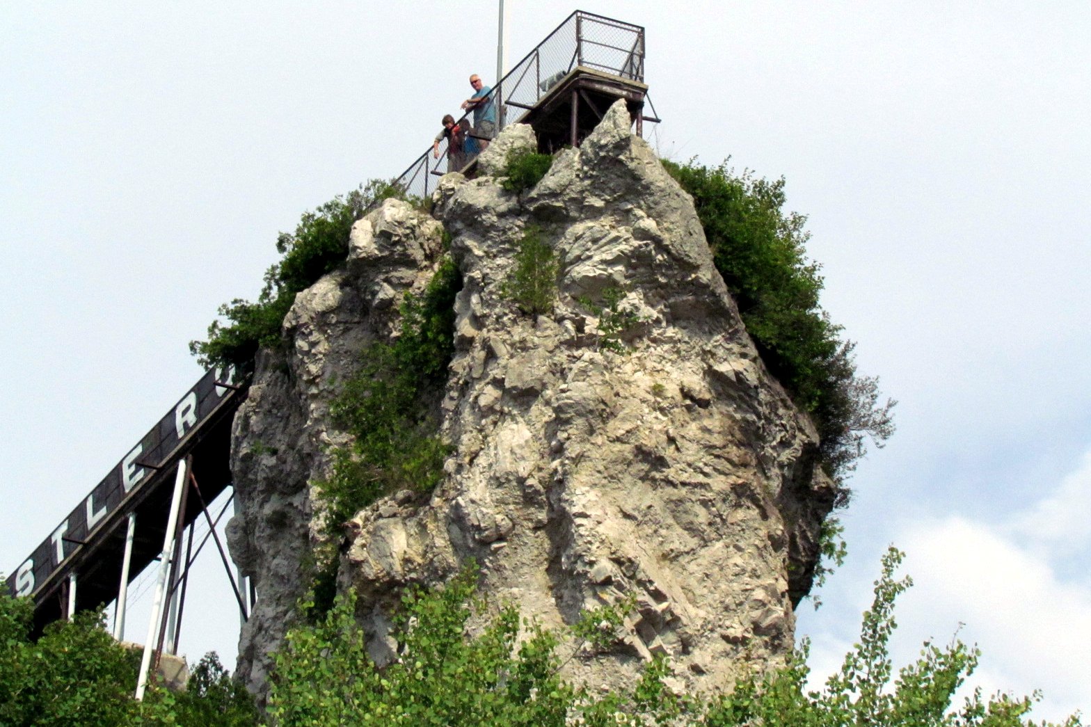 A tall, craggy limestone rock with trees growing on it and a wooden staircase and railed lookout platform at the top.