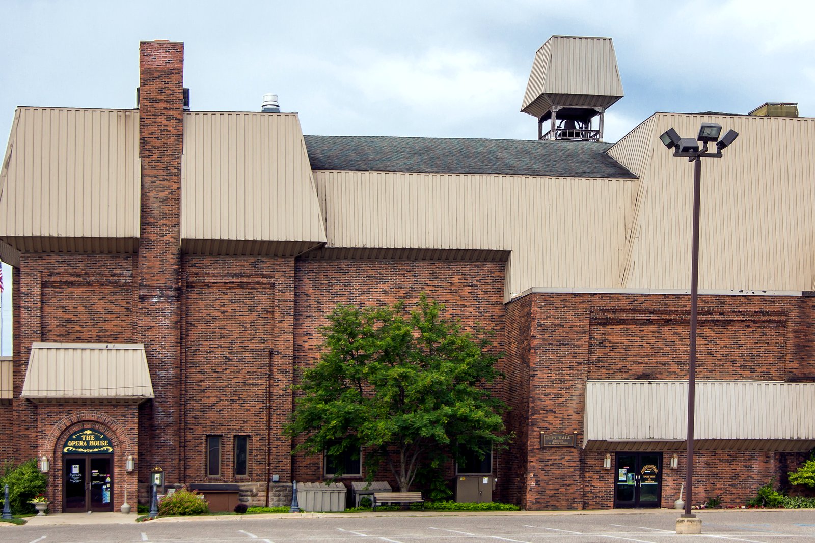 The brick Cheboygan Opera House with tan metal roofs, an arched front entrance and a cupola, seen from its parking lot.
