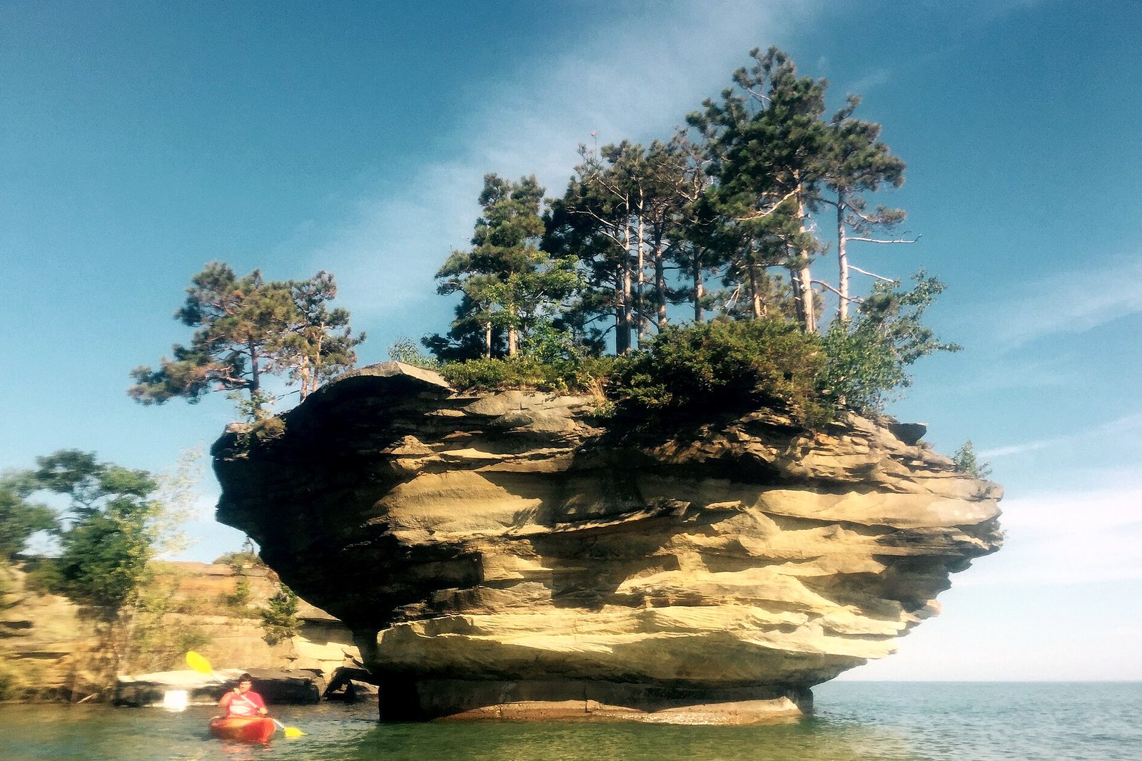 Turnip Rock, a sandstone stack topped with small trees, rising from clear Lake Huron water off Pointe aux Barques, with a red kayak nearby.