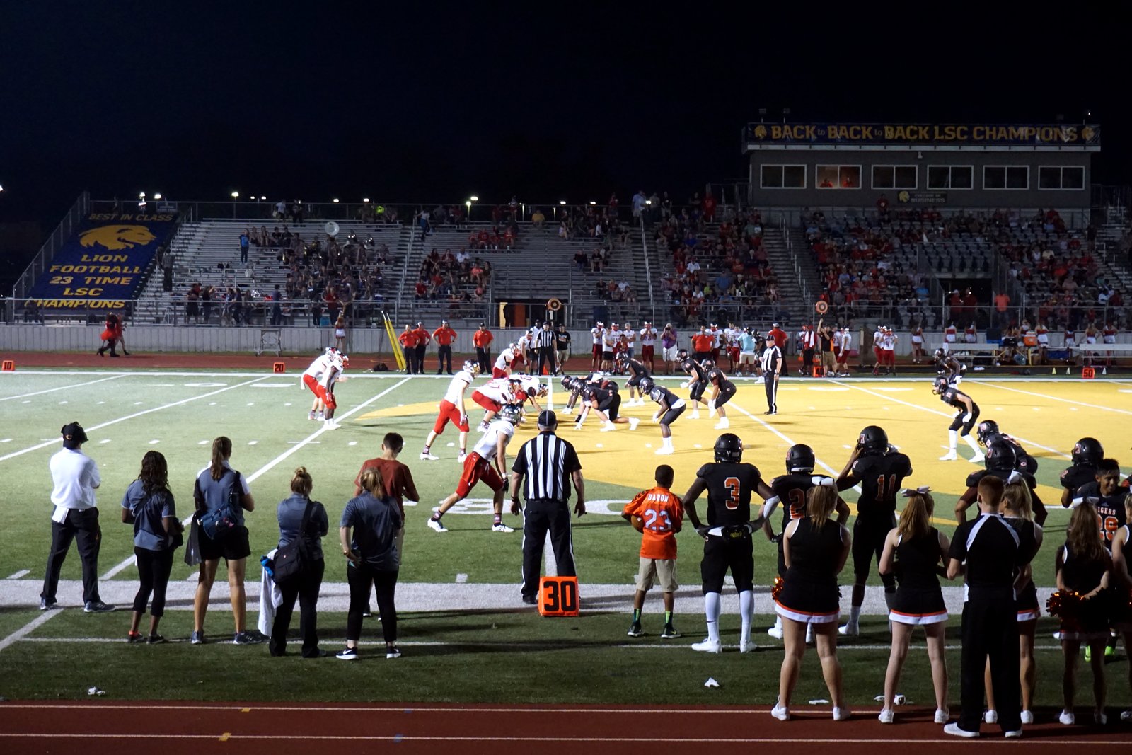 High school football players in dark and white uniforms line up at the line of scrimmage under stadium lights, in a file photo.