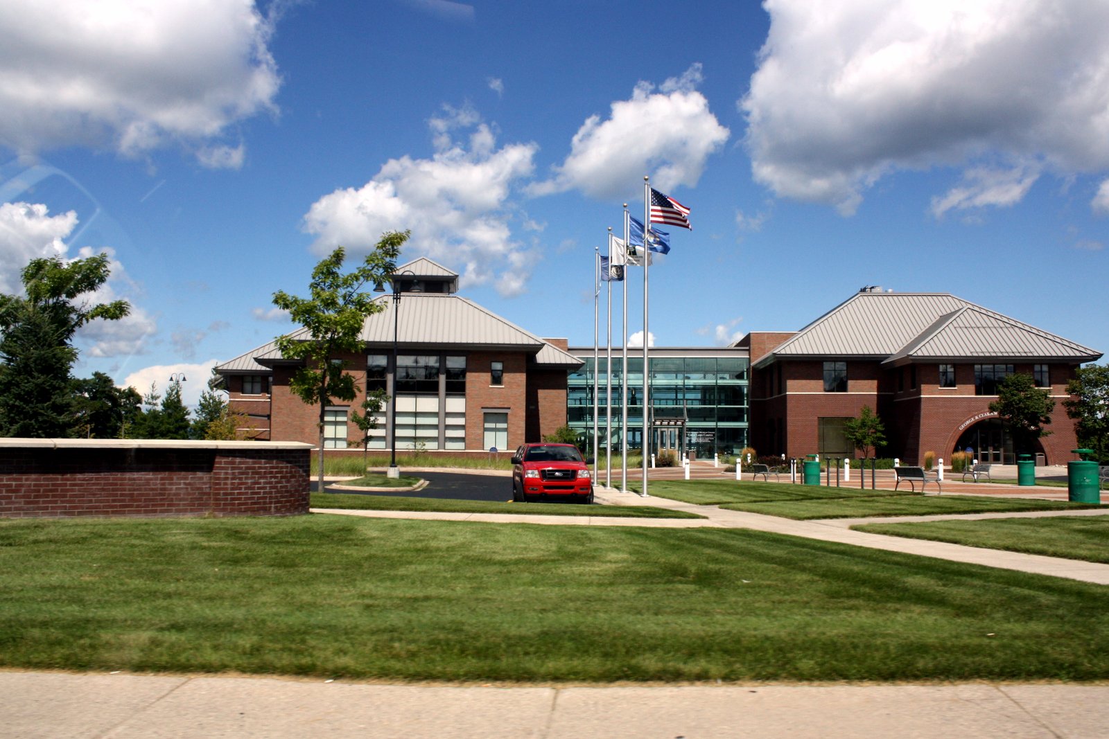 A low brick and glass college building with a green lawn and trees under a blue sky.