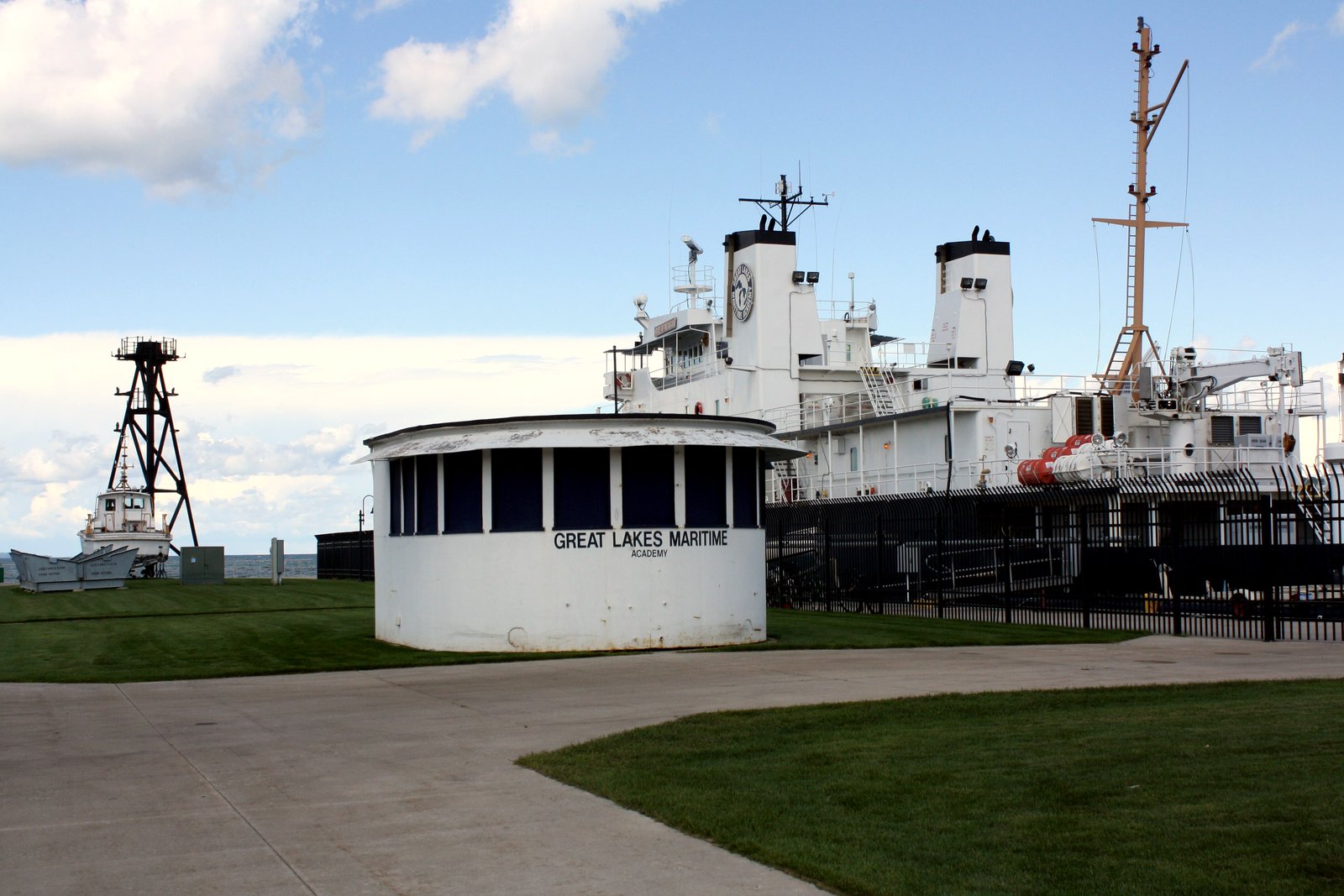 A small round white building with a lawn and walkway in front of it, and a large white ship docked behind.