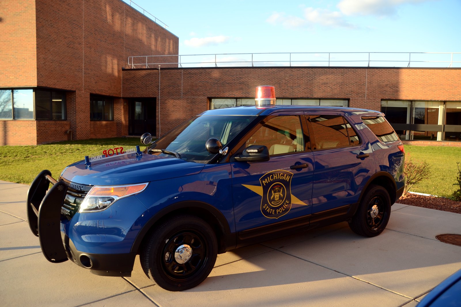 A blue Michigan State Police Ford Explorer patrol vehicle parked outside a brick building.