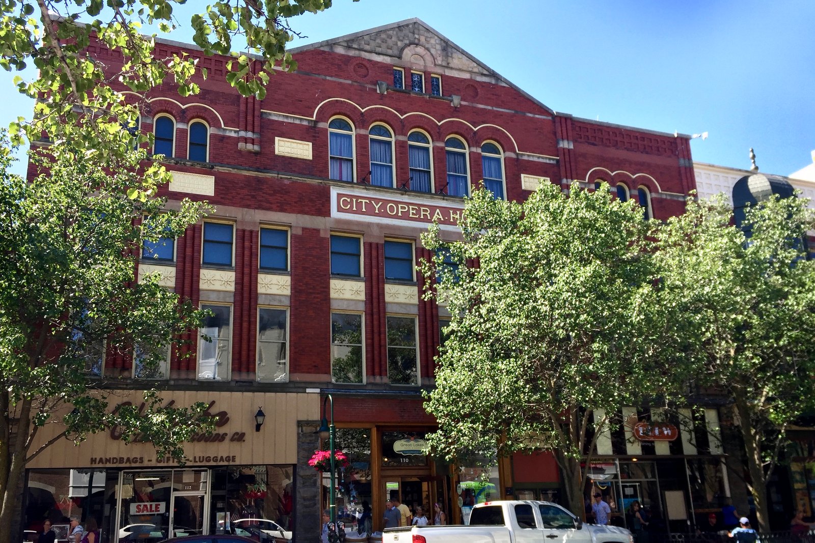 A tall red-brick Romanesque building with arched windows and a ground-floor storefront on a downtown street, with flags hanging along the facade.