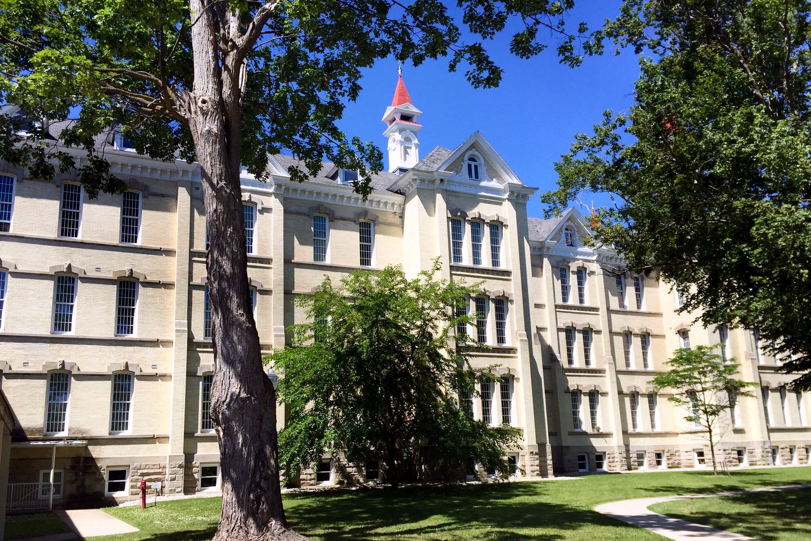 A large cream-brick Victorian building with steep roofs, spires and rows of tall windows, behind a lawn and trees.