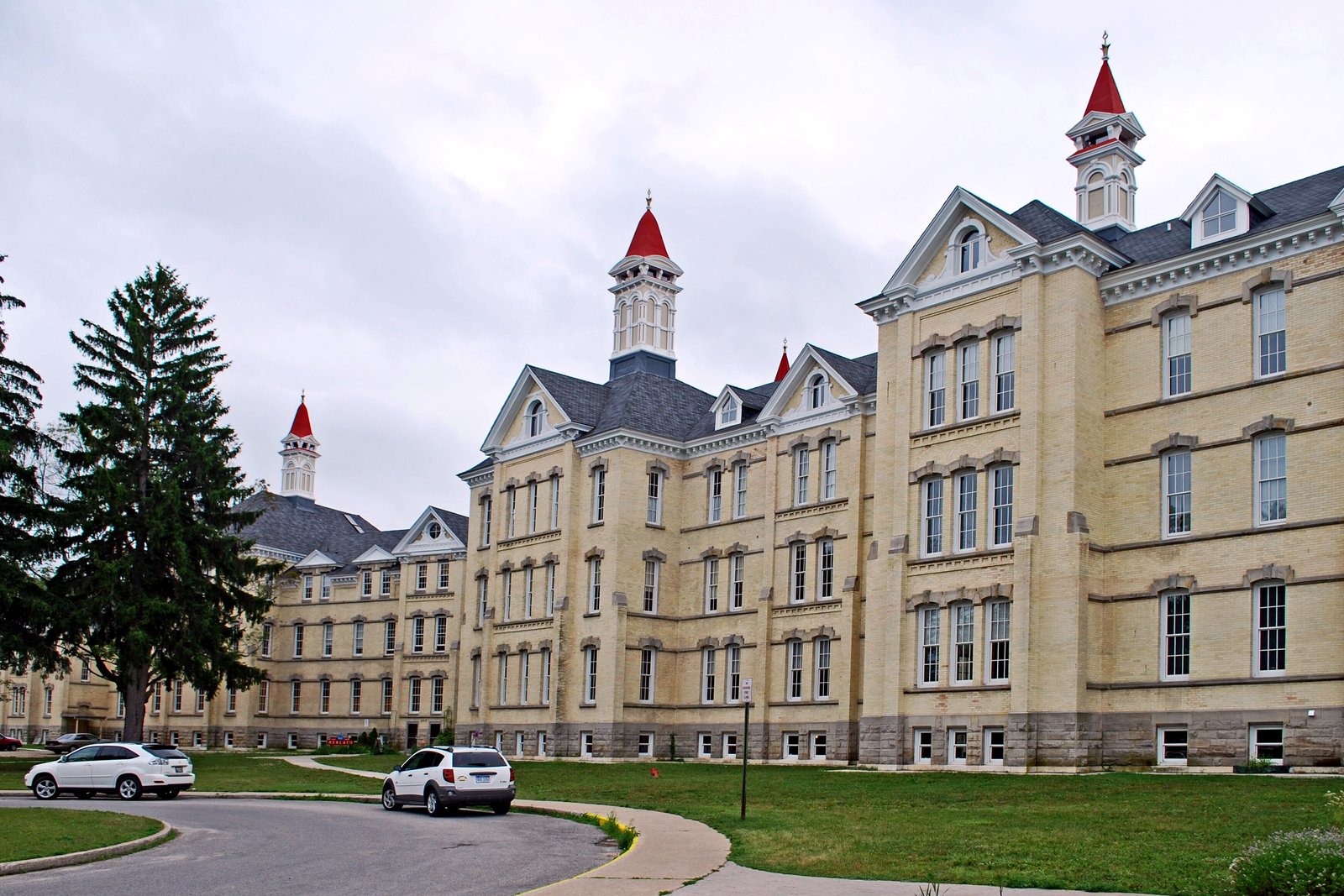 A huge cream-colored brick Victorian building with steep red roofs and pointed towers rising over trees and a lawn.