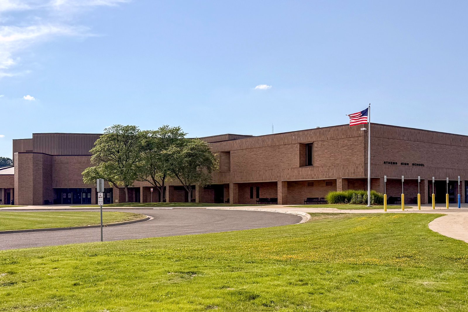A long, low tan-brick high school with an American flag, a curving driveway and a green lawn in front.