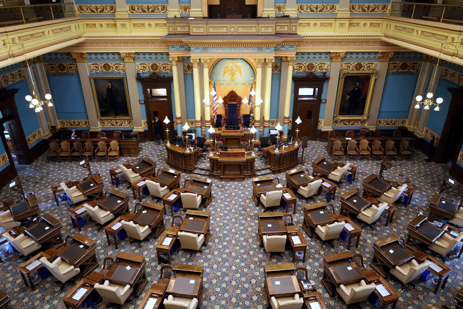 The Michigan Senate chamber in the State Capitol, with rows of wooden desks and chairs under an ornate ceiling and gold-trimmed walls.