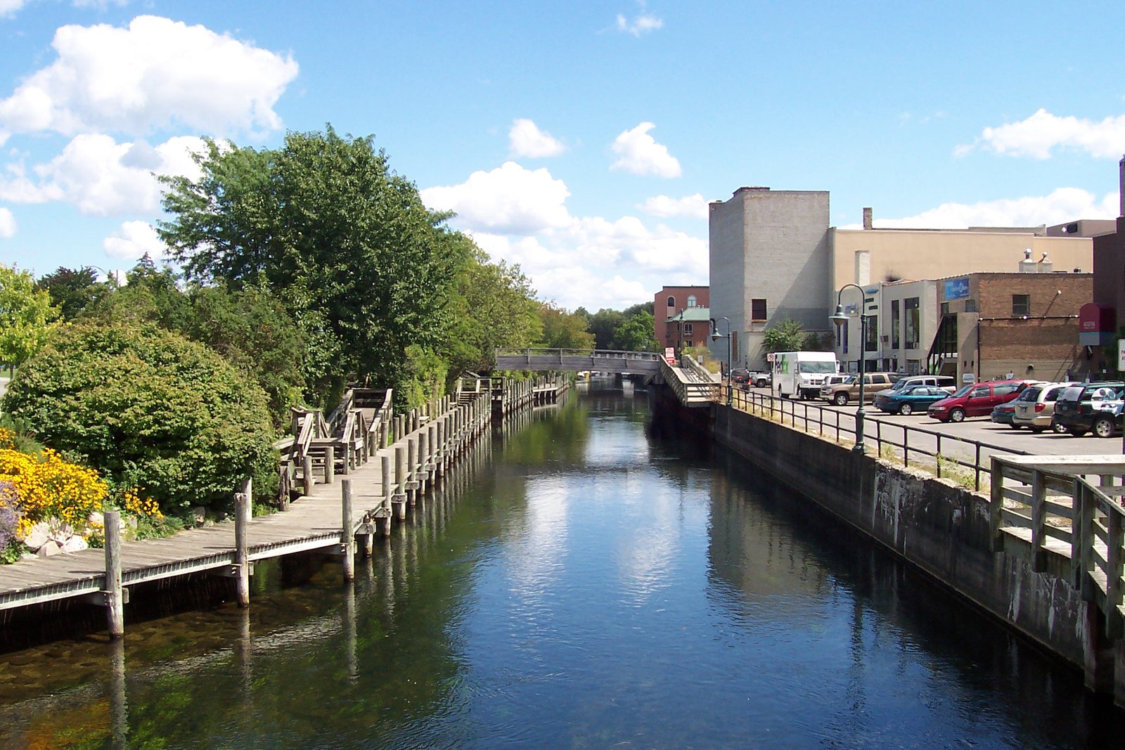 The Boardman River flowing between wooden boardwalks and trees through downtown Traverse City, with buildings in the background.