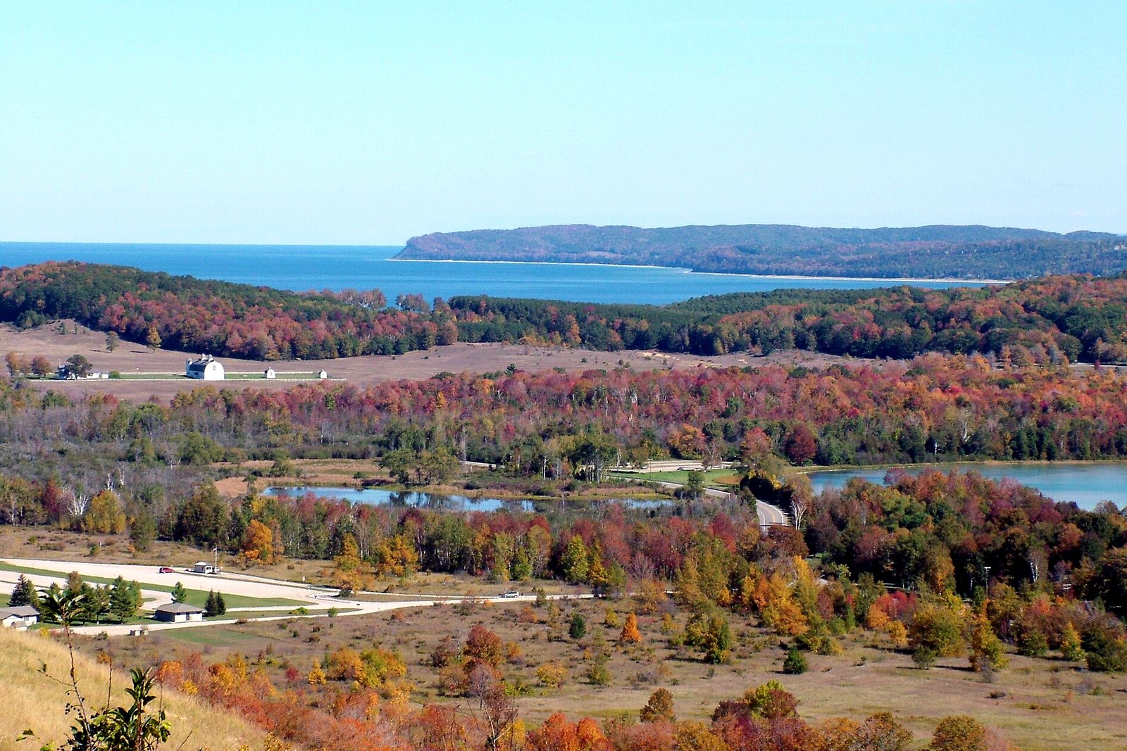 Fall color in red, orange and gold around Glen Lake, with M-109 and Sleeping Bear Bay beyond, seen from Sleeping Bear Dunes National Lakeshore.