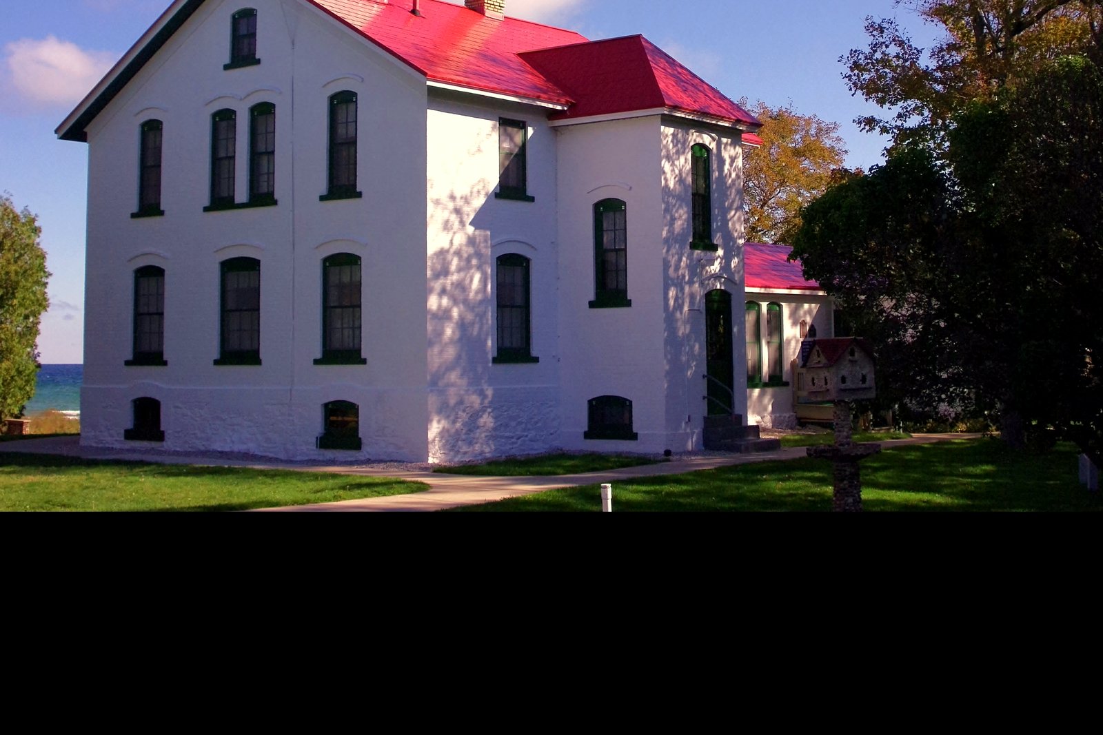 The white brick Grand Traverse Lighthouse with its red roof and lantern room standing near Lake Michigan trees.