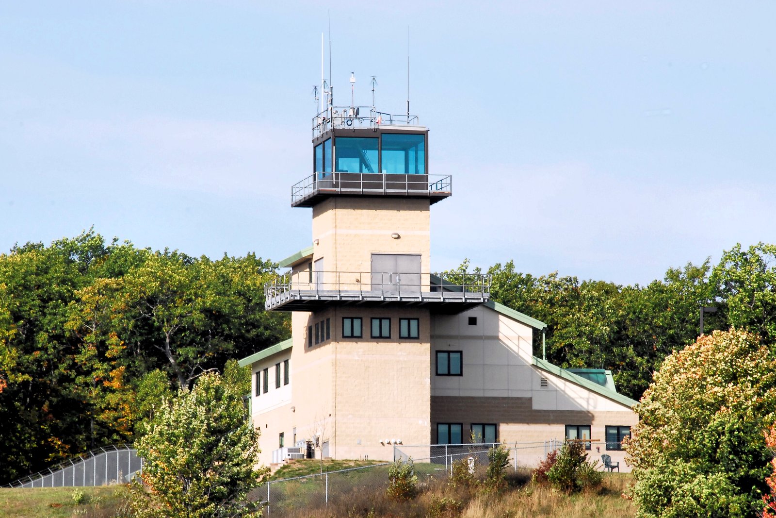 A tall range control tower with a glass observation deck rises above fall-colored trees.