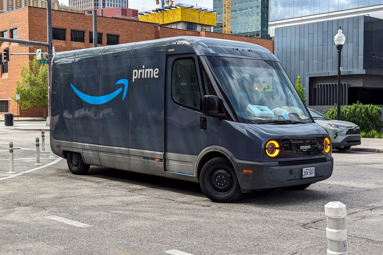 A dark gray electric delivery van with blue Amazon prime branding on a city street.