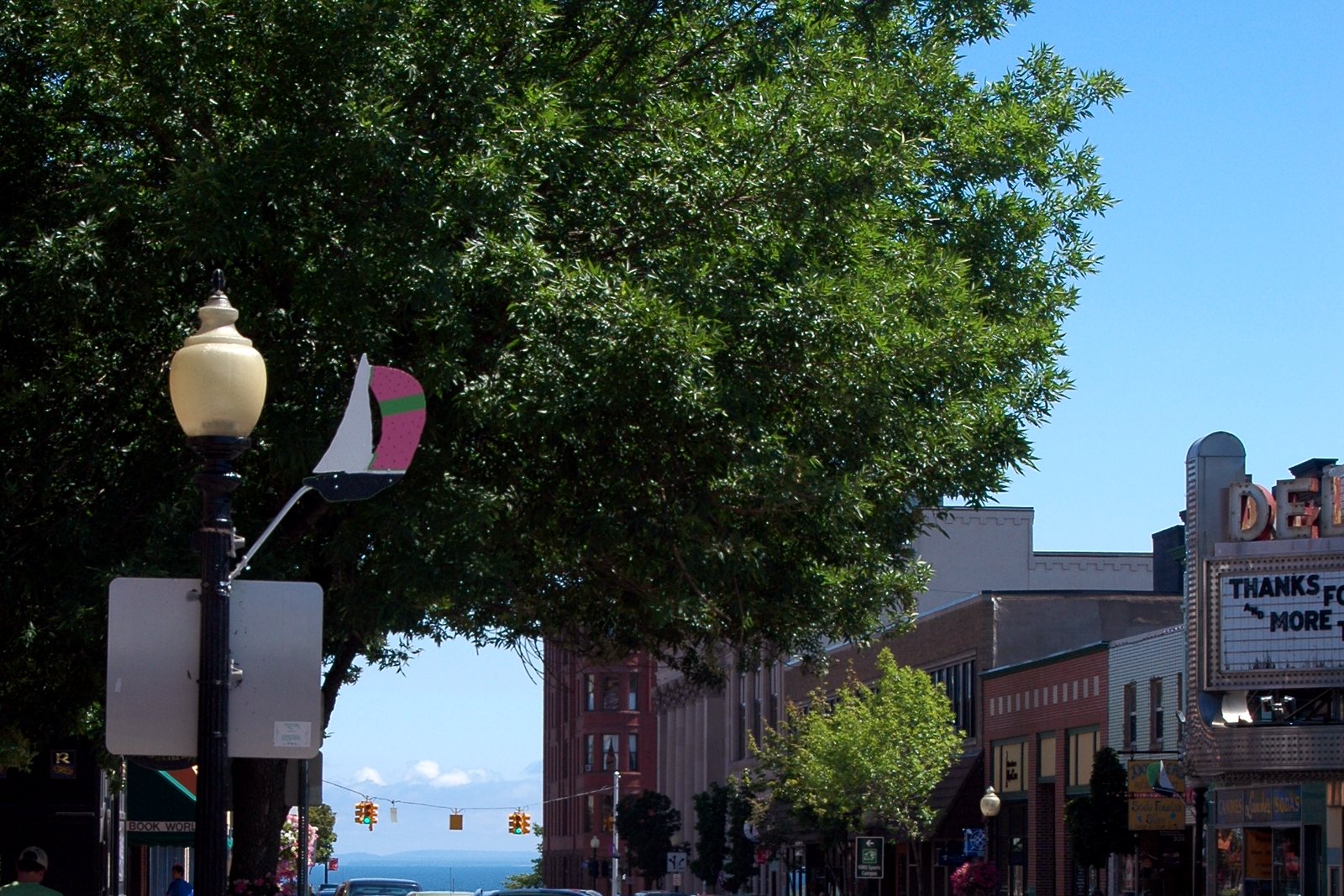 A tree-lined downtown street with brick storefronts, a theater marquee and Lake Superior in the distance in Marquette.
