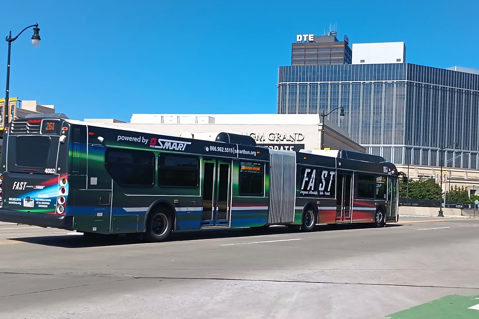 A blue, white and red articulated SMART FAST bus driving past modern office buildings on a sunny day.