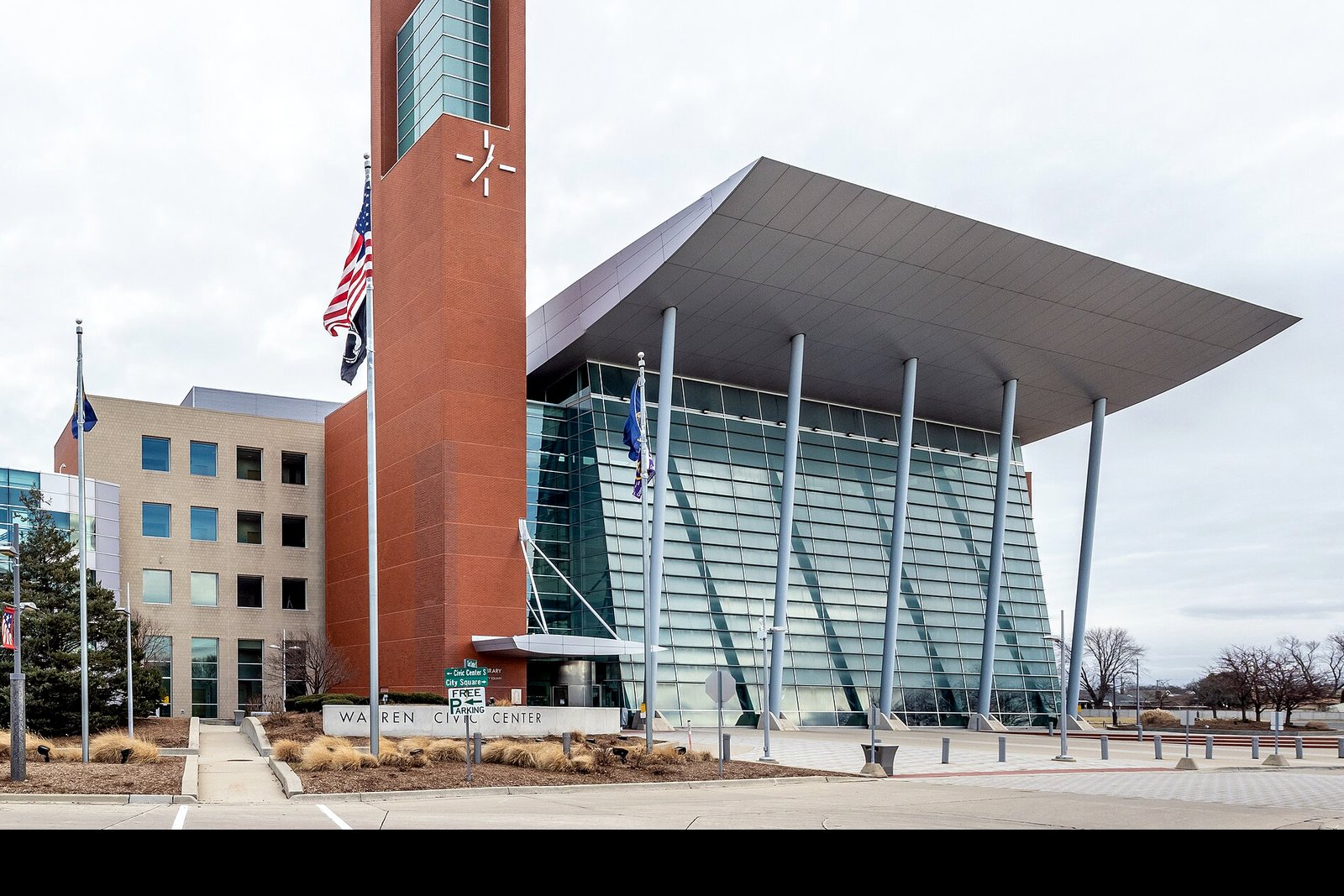 The glass-fronted Warren Civic Center rises above a plaza with planters and a circular drive on a clear day.